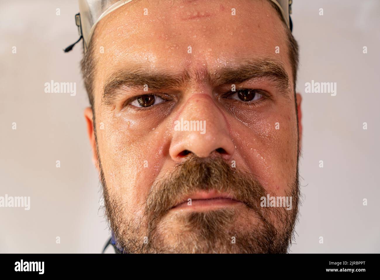 Mise au point sélective, gros plan de visage d'homme sueur, épuisé avec des marques d'équipement de sécurité. Banque D'Images