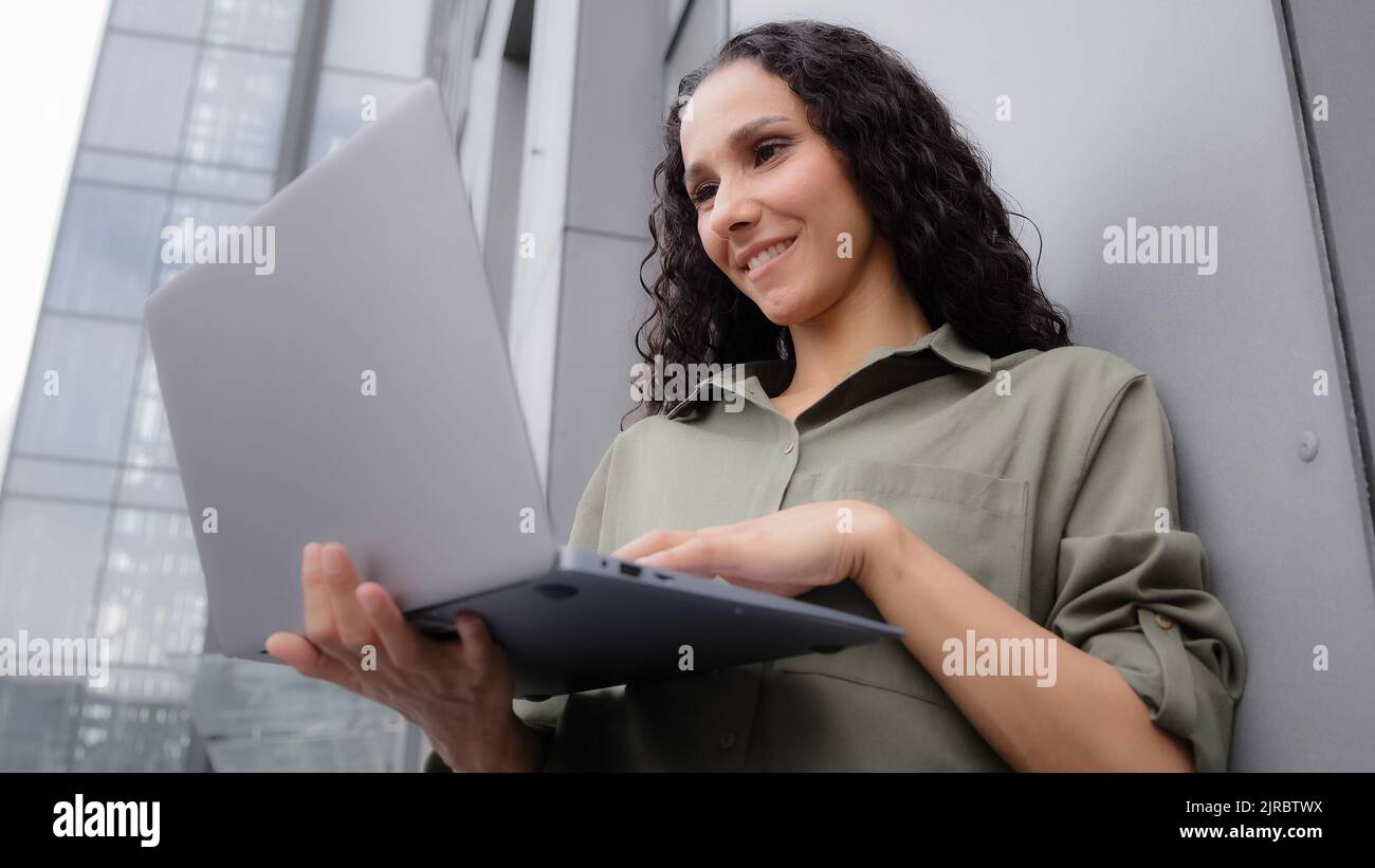 Gros plan occupé commerçant souriant architecte femme d'affaires patron utilisateur femme investisseur dame penchée mur à l'extérieur près de l'entreprise bâtiment travaillant taper sur Banque D'Images