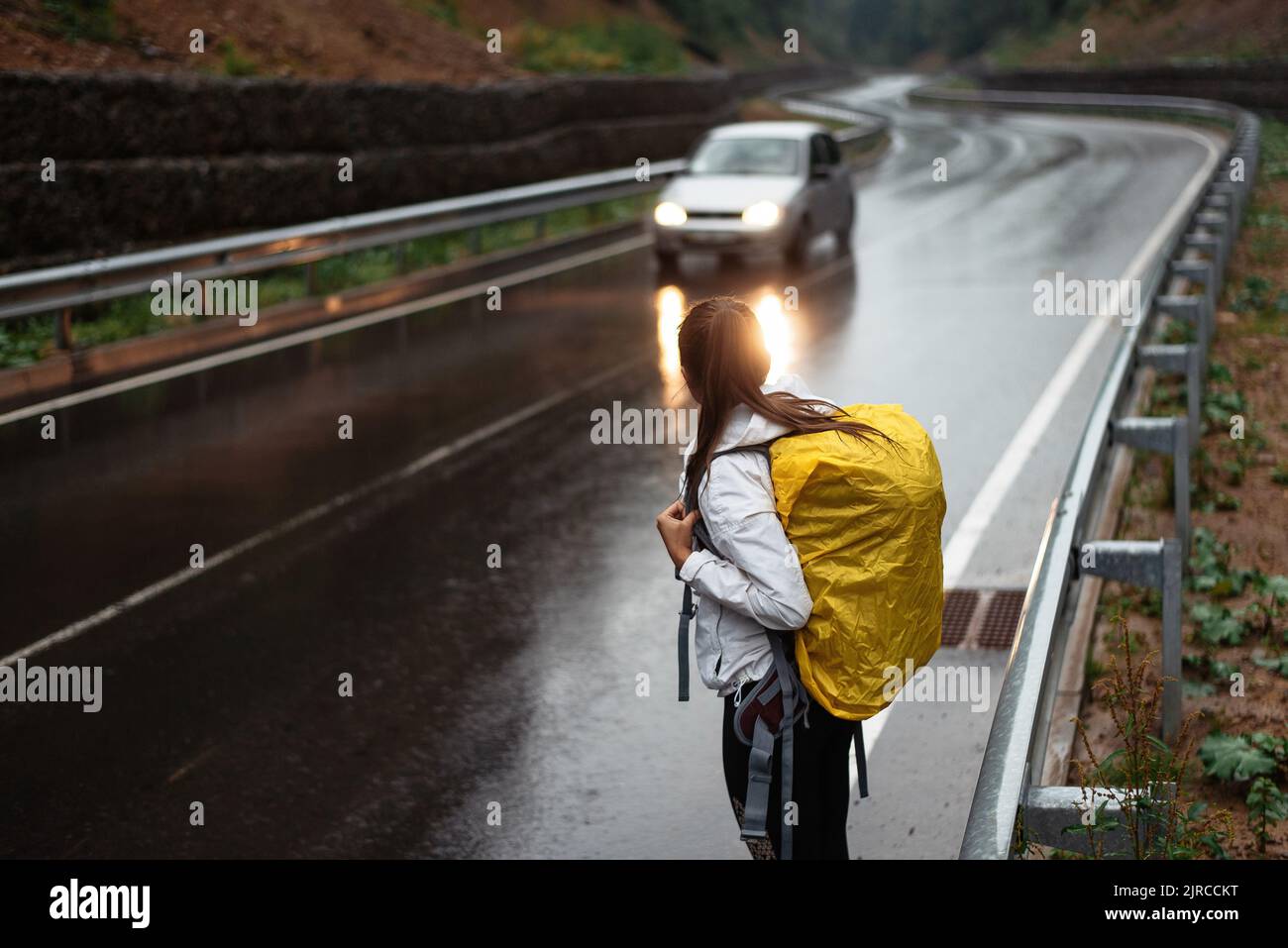 Une femme qui cherche à se départir en attendant des voitures avec un sac à dos jaune dans la nature. Happy girl est trekking sur la route de la forêt avec sac à dos de camping. De voyage Banque D'Images