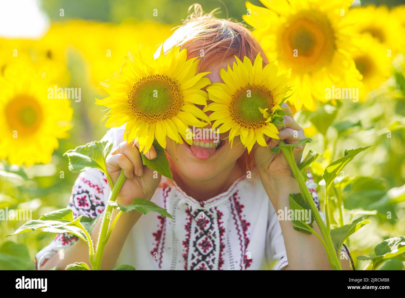 fille en broderie hid les yeux derrière les tournesols. Femme heureuse parmi les fleurs jaunes. Le jour de l'indépendance de l'Ukraine. Vêtements nationaux de l'Ukraine. Banque D'Images