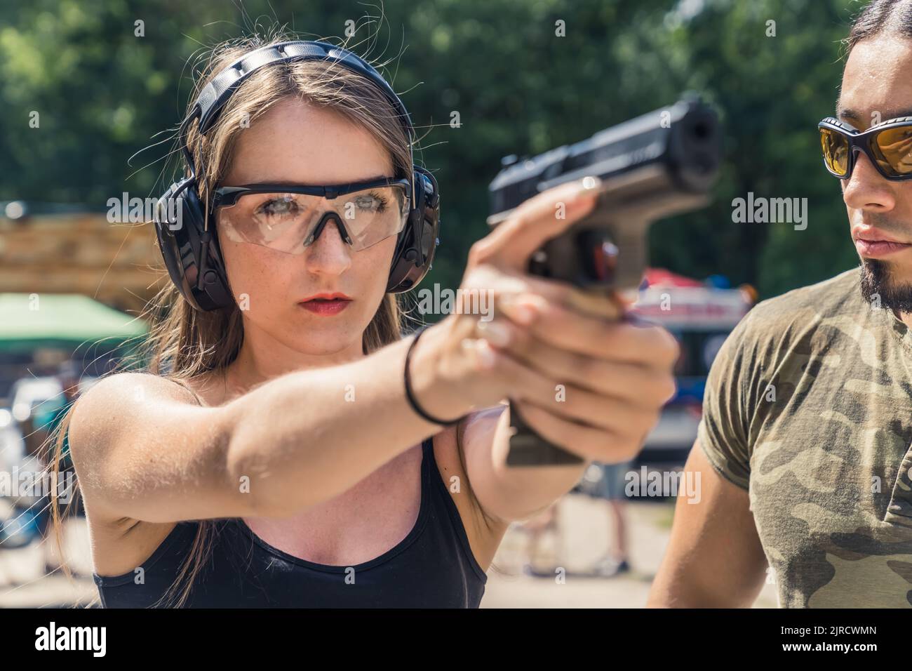Jeune femme caucasienne portant des lunettes de protection et des écouteurs visant le pistolet observé par un instructeur barbu. Formation sur les armes à feu. Tir Horiozntal. Photo de haute qualité Banque D'Images