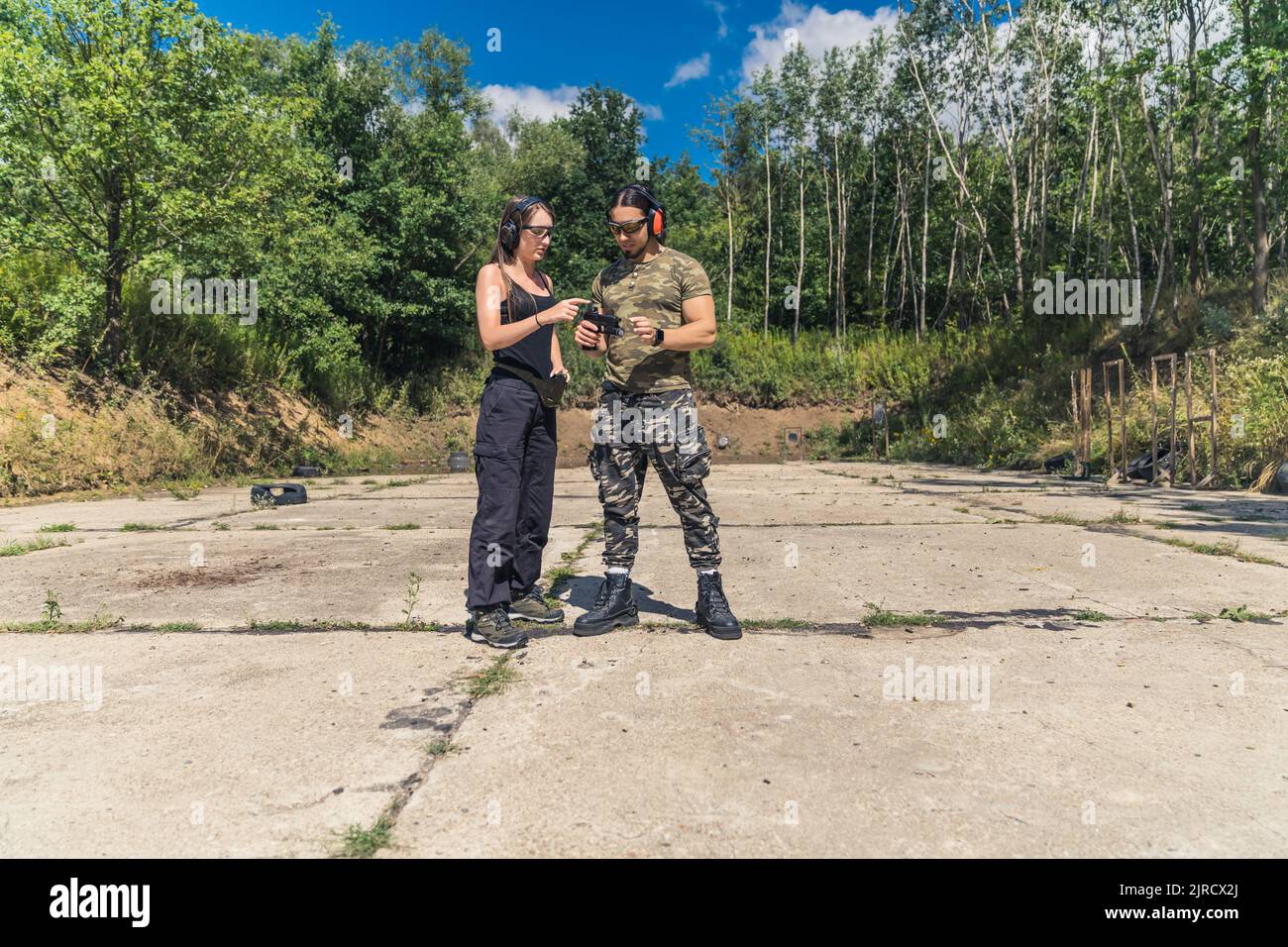 Femme en vêtements noirs montrant l'homme en vêtements de camouflage comment faire fonctionner le pistolet à main. Client avec instructeur à la portée de tir. Prise de vue horizontale en extérieur. Photo de haute qualité Banque D'Images