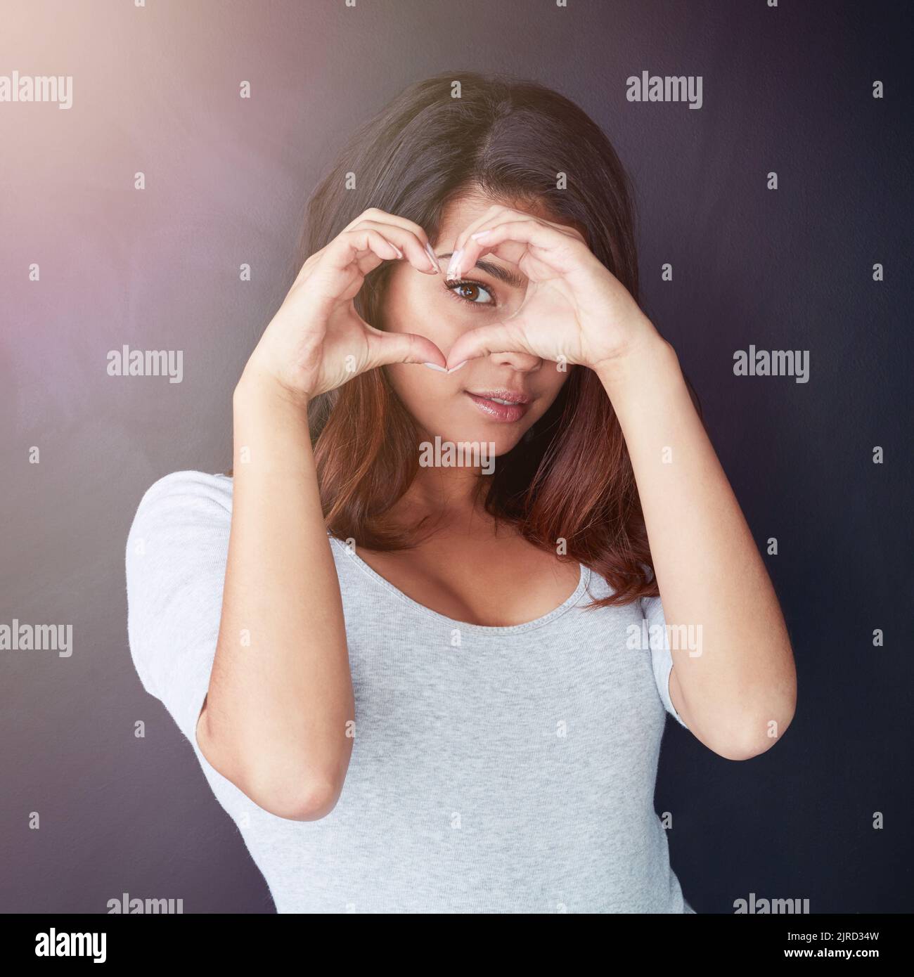 Tout voir par l'amour. Portrait d'une belle jeune femme regardant à travers ses mains en forme de cœur dans le studio. Banque D'Images