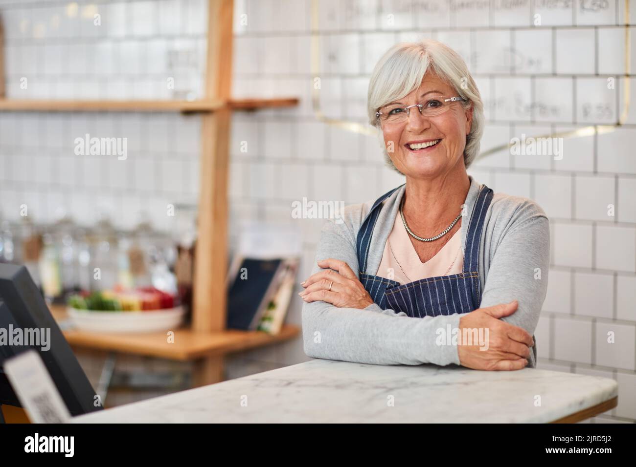 Mon café est mon endroit heureux. Portrait d'un propriétaire d'entreprise senior heureux qui se pose au comptoir dans son café. Banque D'Images