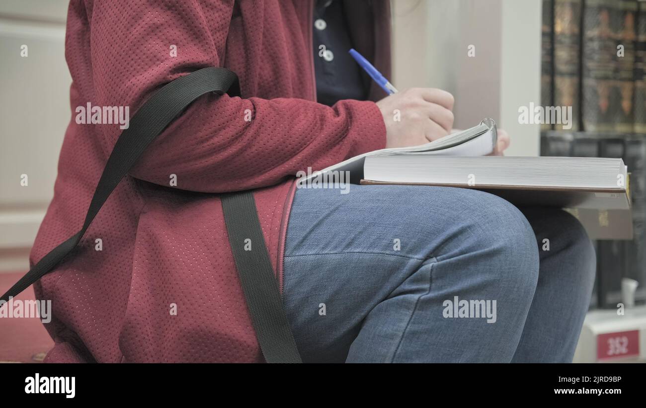 Une femme portant des lunettes et un masque est assise sur les marches de la bibliothèque lit le livre, prenant des notes Banque D'Images