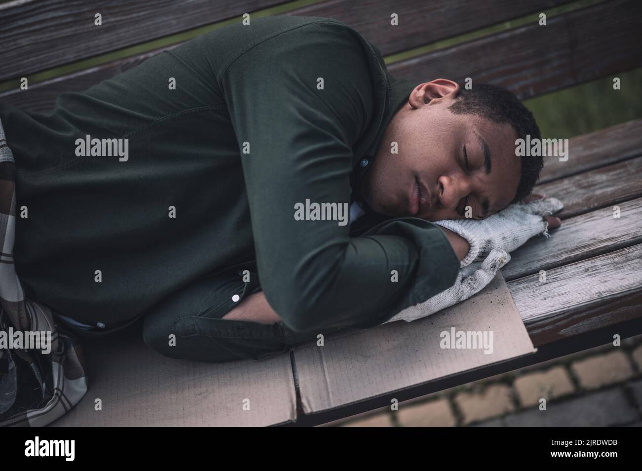 Homme à la peau sombre dormant sur un banc en carton Banque D'Images