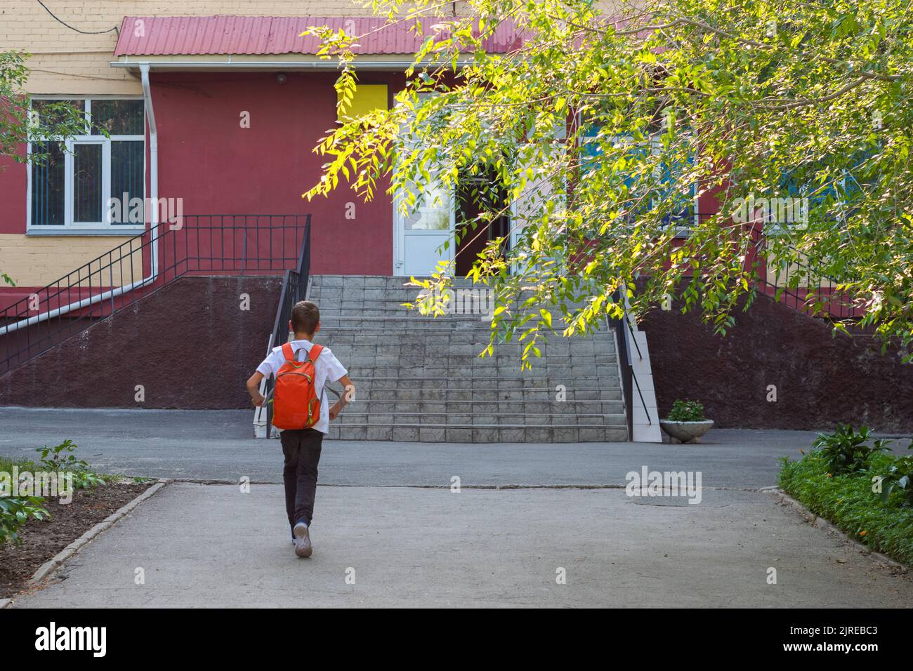 Un enfant souriant va à l'école. Vue arrière d'un garçon marchant dans les escaliers à l'extérieur de l'arrière-plan du bâtiment. Un étudiant va étudier avec un sac à dos. Arrière t Banque D'Images