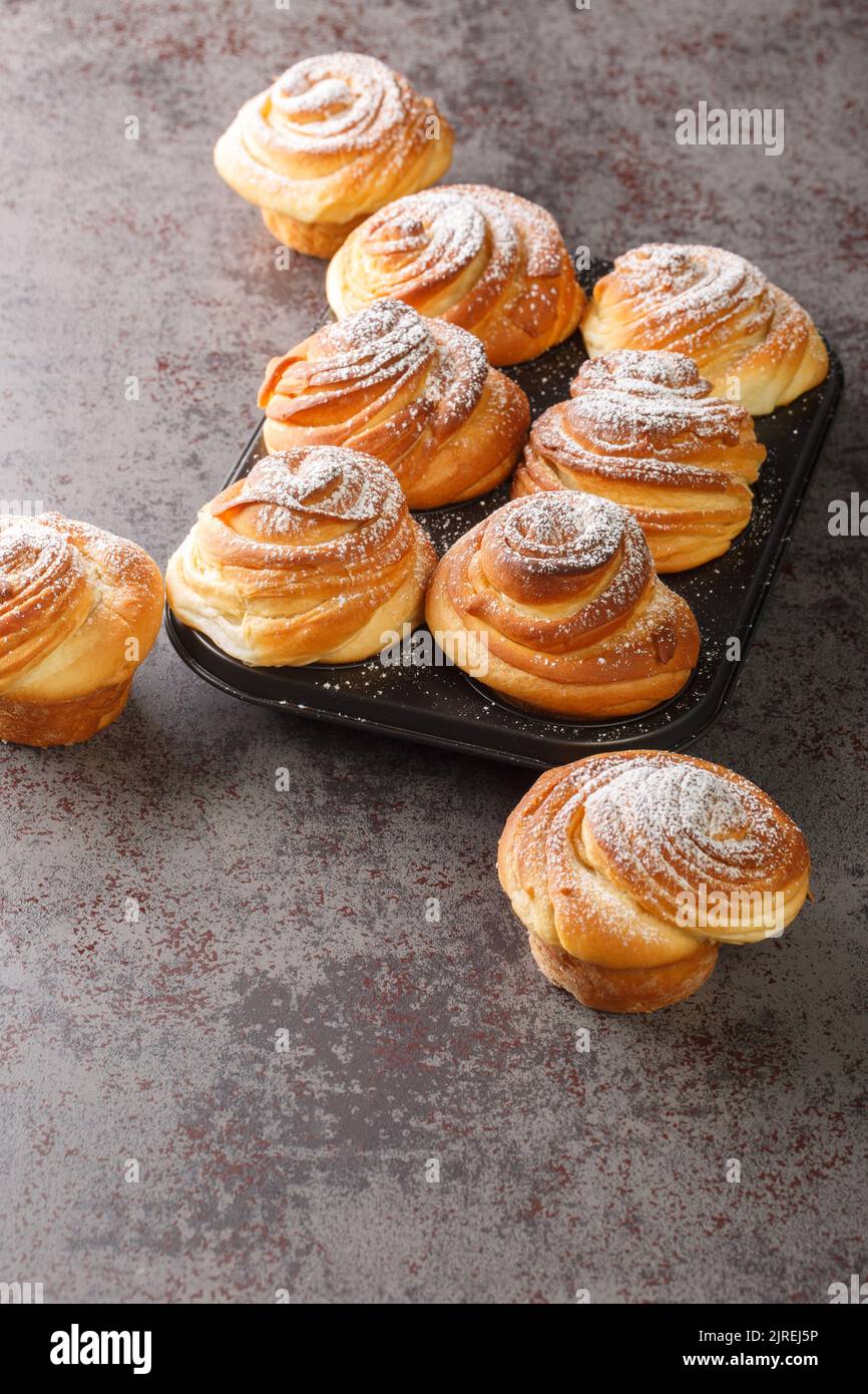 Croûtes de pâtisserie modernes croissants sous forme de muffin saupoudrés de sucre en poudre sur fond sombre, dans le moule à muffins de la table. V Banque D'Images