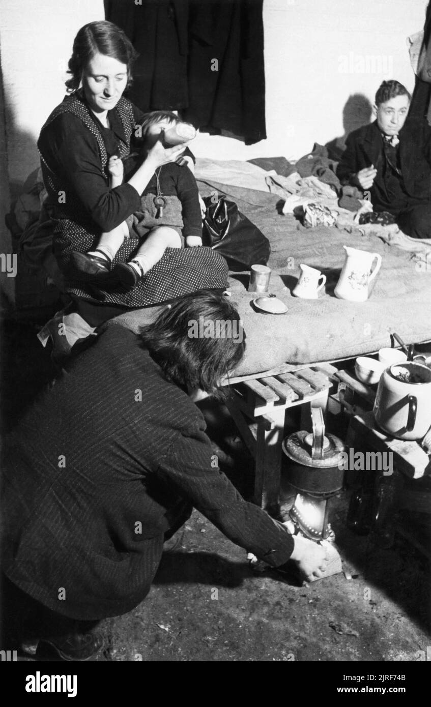 Bouteille d'une mère nourrit son bébé sur un lit de fortune dans un abri anti-aérien sous les arches de chemin de fer dans le sud-est de Londres au cours de 1940. Bouteille d'une mère nourrit son bébé sur un lit de fortune dans l'abri sous le chemin de fer d'arches, quelque part dans le sud-est de Londres. Au premier plan, une autre femme allume la cuisinière de Primus en vertu de l'électrique, prêt à faire une tasse de thé. Cette photographie a probablement été prise en novembre 1940. Banque D'Images