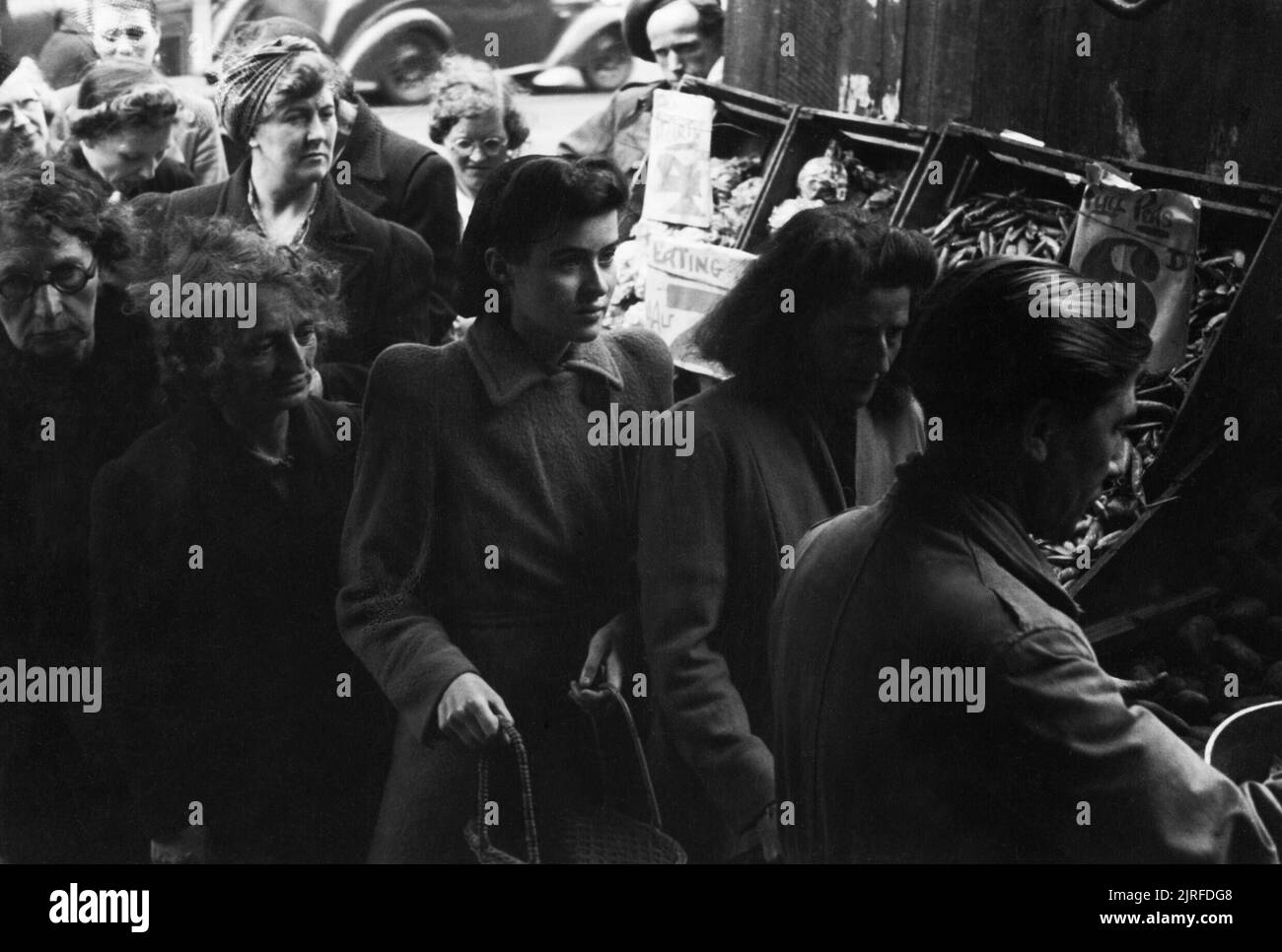 File d'attente des femmes pour les pommes de terre à un marchand de shopping à Londres au cours de 1945. Les femmes d'attente pour les pommes de terre dans un marchand de boutique, quelque part dans Londres. Un affichage de haricots peuvent seulement être vu à droite de la photographie. Les jardiniers peuvent seulement être vu servir un client dans le coin inférieur droit. Banque D'Images