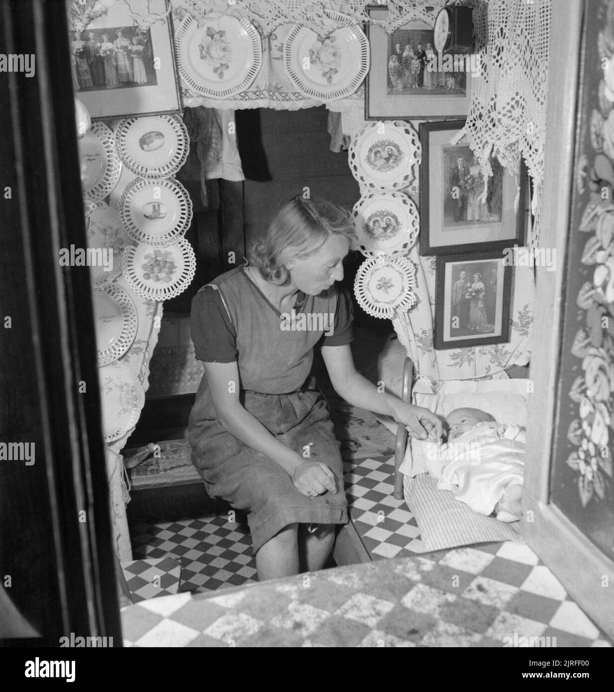 Canaux britanniques en temps de guerre- Transports en Grande-Bretagne, 1944 Une mère installe son bébé pour dormir dans la cabine de son bateau. La cabine est orné d'assiettes décoratives, des photographies de famille et de la dentelle, qui, selon la légende "original sont les caractéristiques d'un bon canal boat cabin'. Banque D'Images