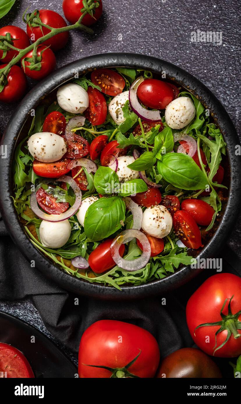 Salade de mozzarella traditionnelle italienne avec des arugula et des tomates sur une table en béton foncé Banque D'Images