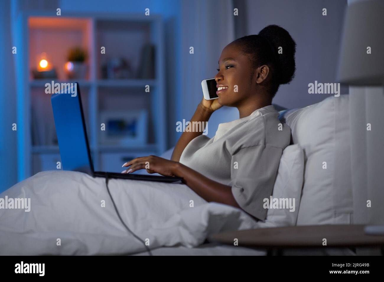 femme avec un ordinateur portable qui appelle sur un smartphone au lit Banque D'Images