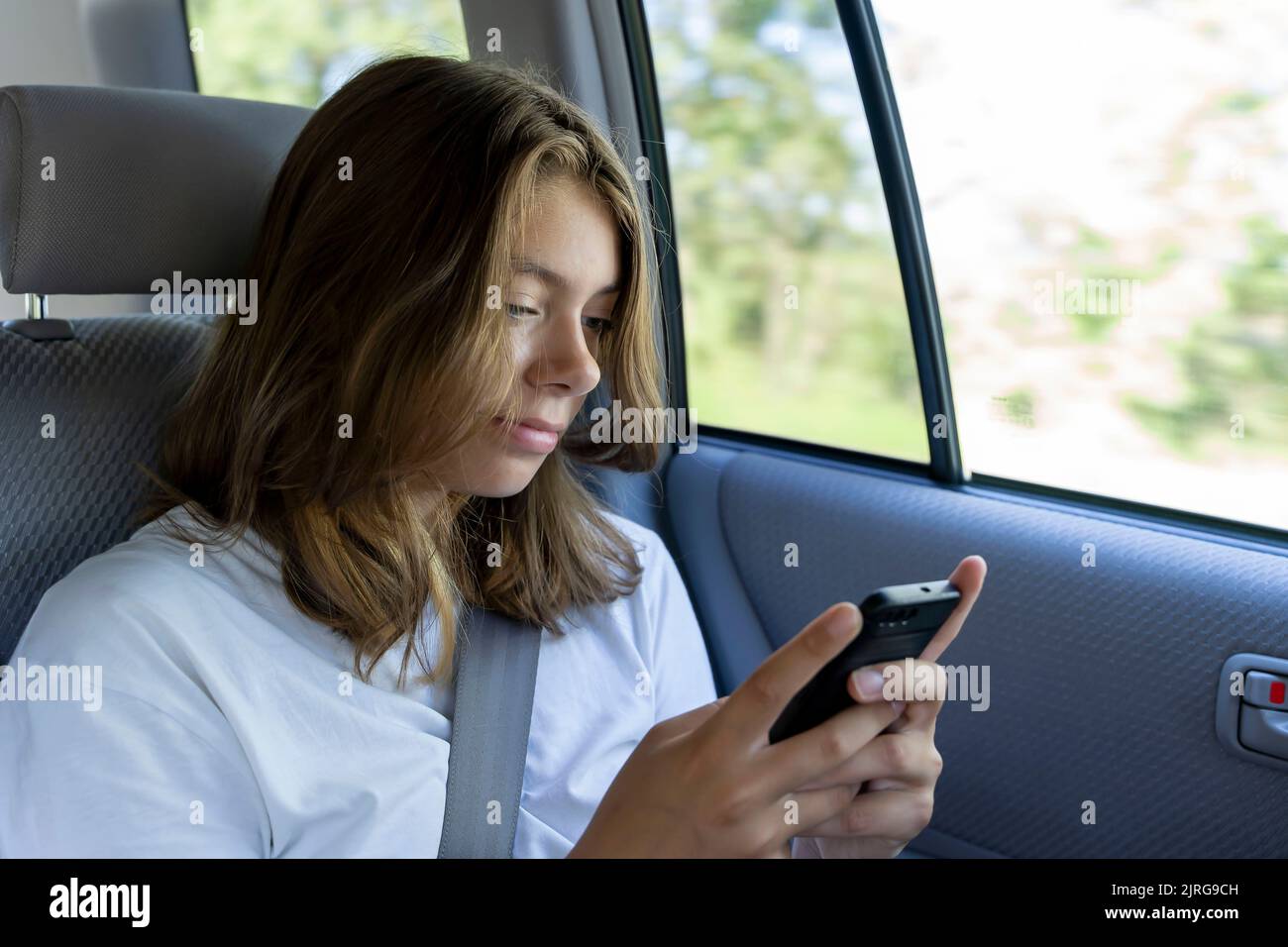 une jeune fille est à cheval dans le siège arrière d'une voiture et utilise un smartphone Banque D'Images