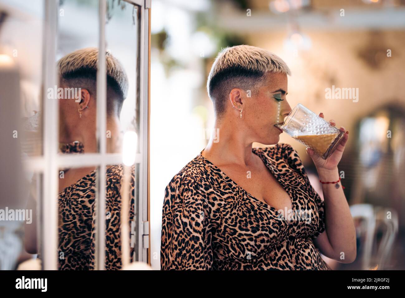 Alternative femme avec les cheveux courts boit une tasse dans un bar et son reflet Banque D'Images