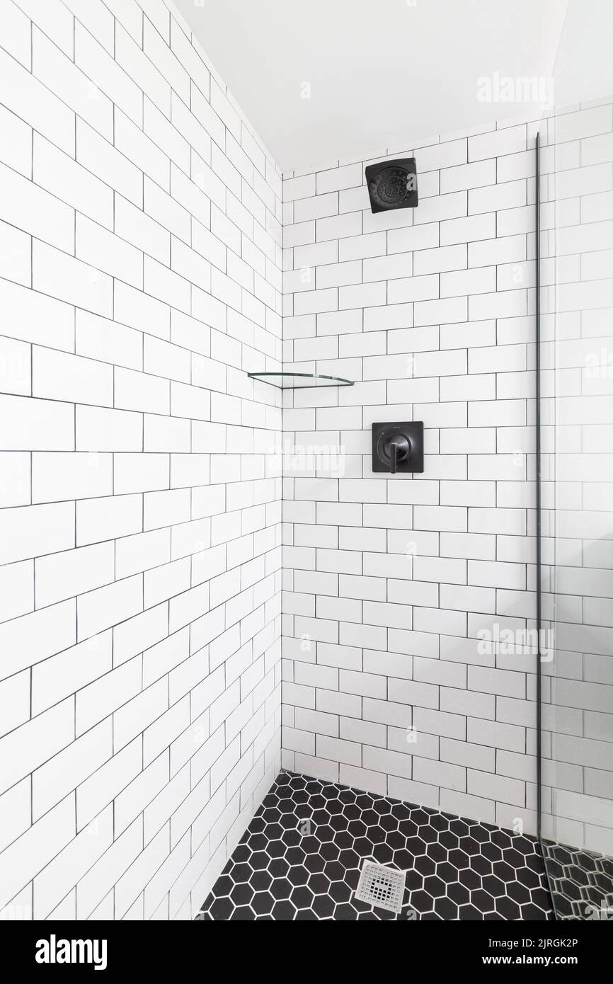 Une douche de métro blanche avec un pommeau de douche noir et un sol en marbre noir. Banque D'Images