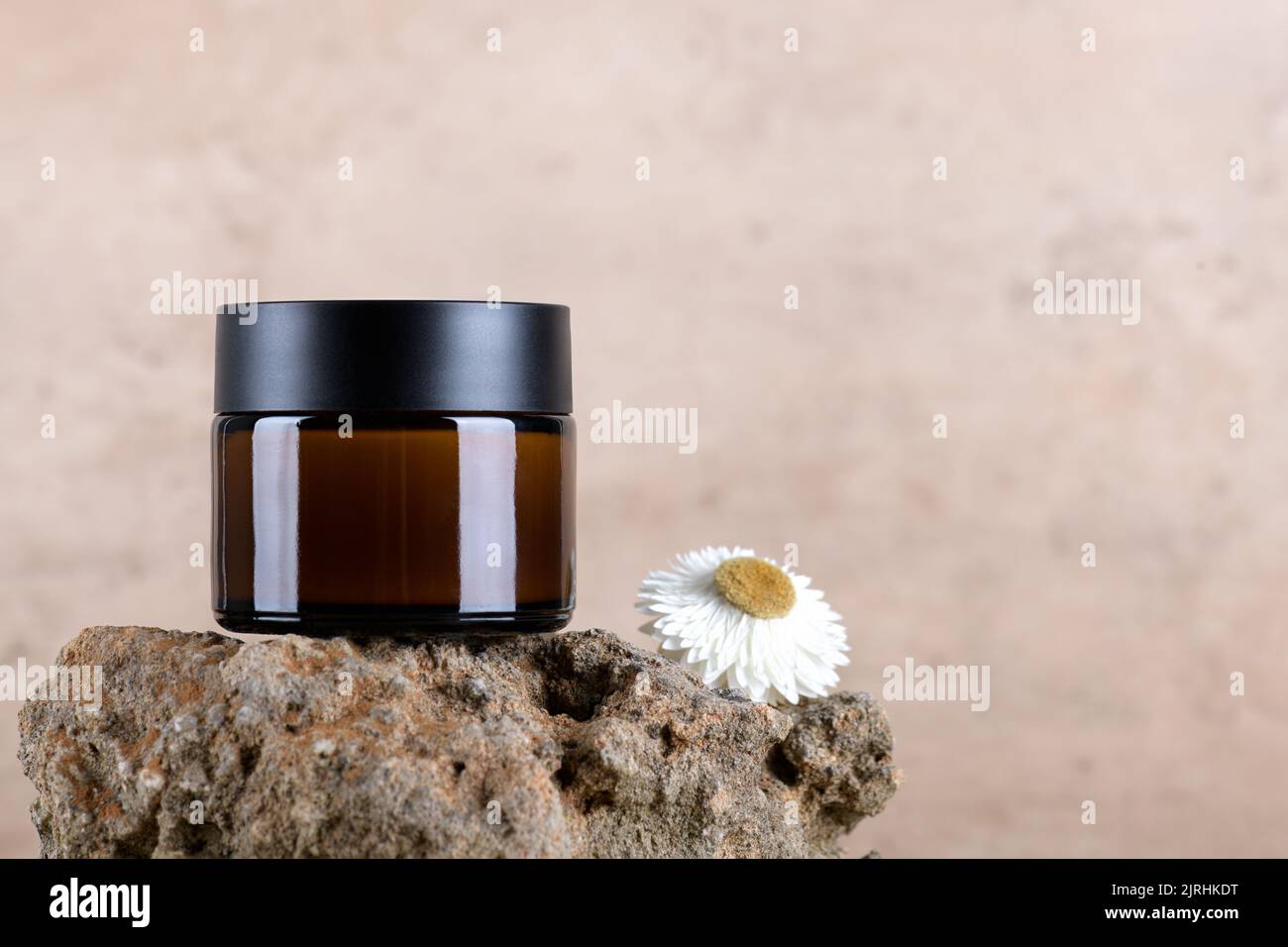 Pot en verre ambré pour crème hydratante sur podium de pierre sur fond beige terre cuite avec fleur sèche. Banque D'Images