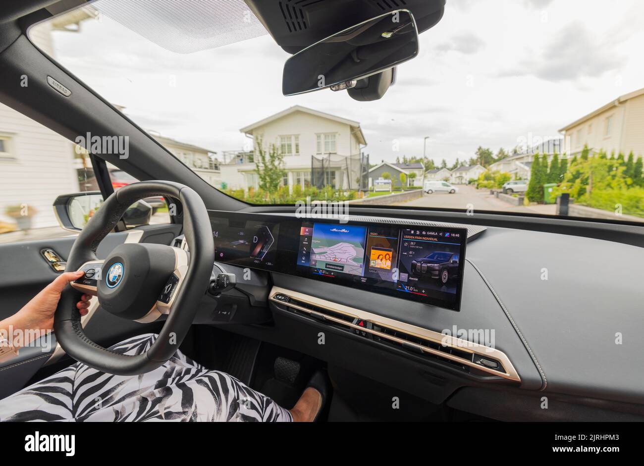 Vue de la femme conduisant une nouvelle BMW iX40 voiture électrique passant par le village de cottage. Suède. Uppsala. Banque D'Images