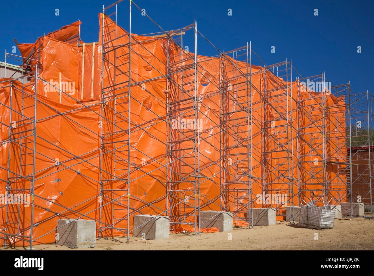 Un bâtiment commercial est recouvert d'une couverture en plastique orange pendant les travaux de rénovation afin de contenir la poussière et les débris. Banque D'Images