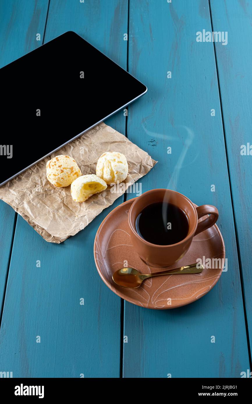 Pains au fromage brésilien à côté d'une tasse de café, d'une cuillère dorée et d'une tablette verticale. Banque D'Images