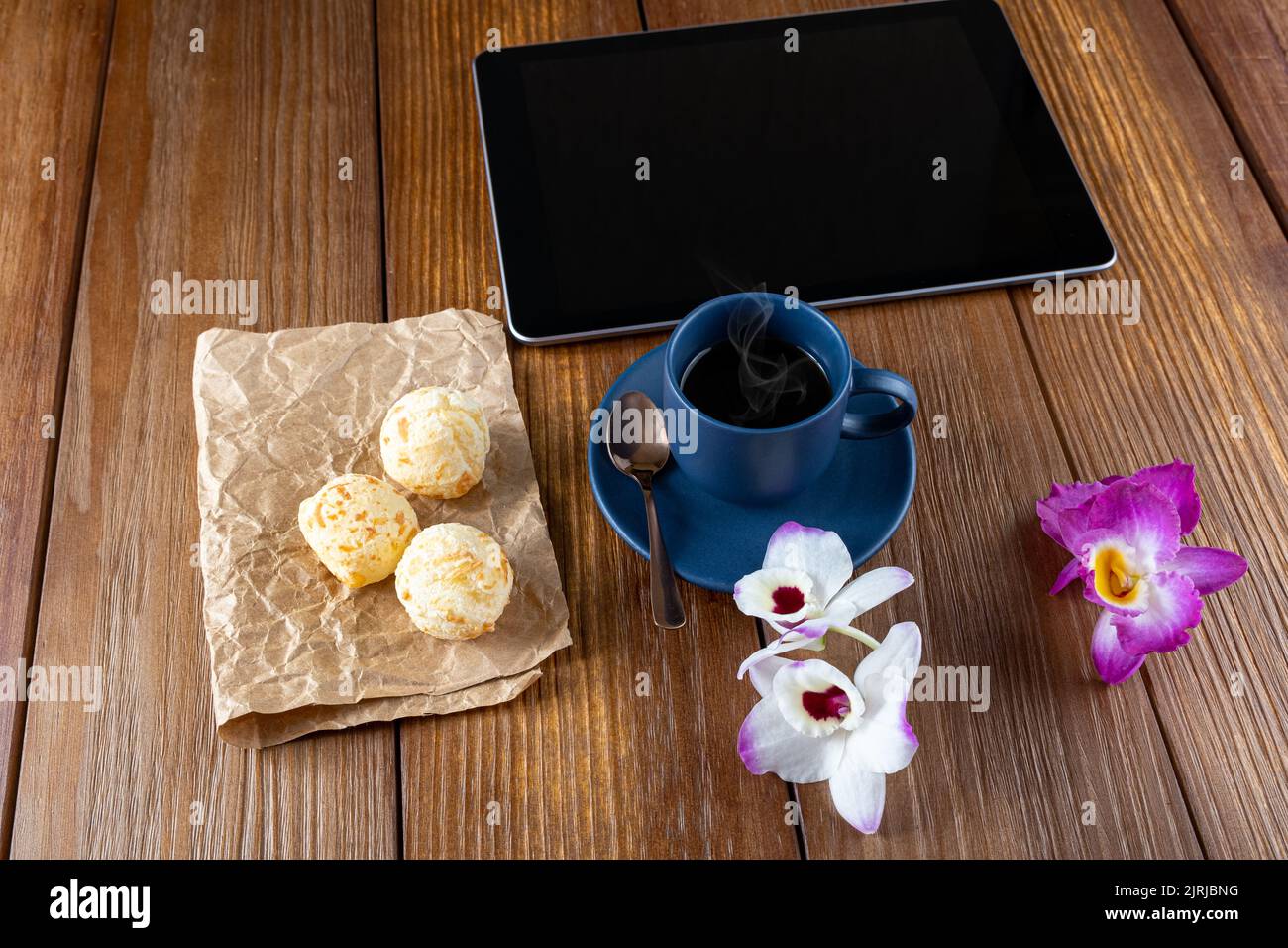 Pains au fromage brésilien à côté d'une tablette, d'une tasse de café, d'une cuillère en cuivre et de fleurs. Banque D'Images