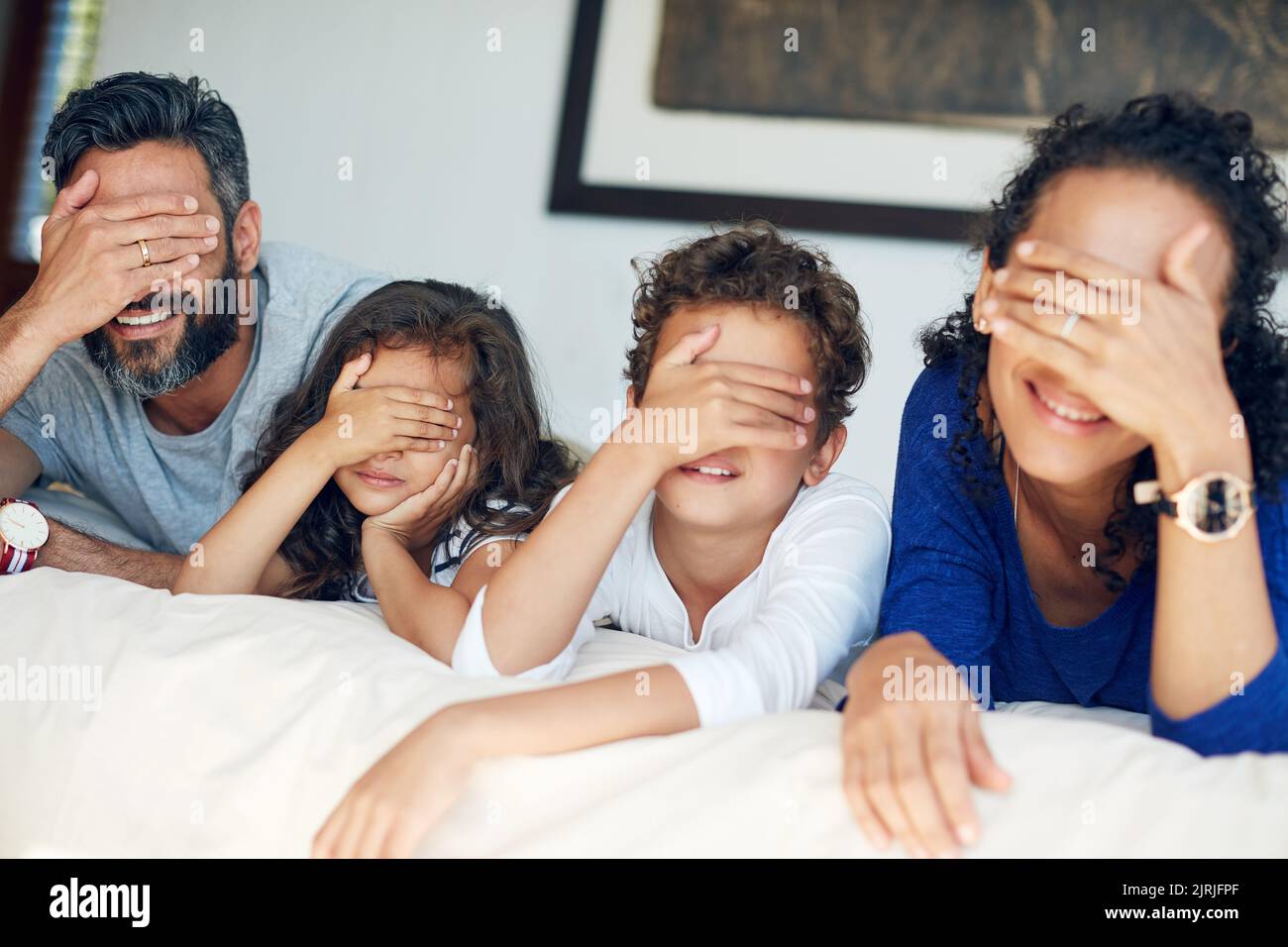 Quelle surprise nous réserve le week-end : une famille qui couvre les yeux tout en étant allongé sur un lit à la maison. Banque D'Images