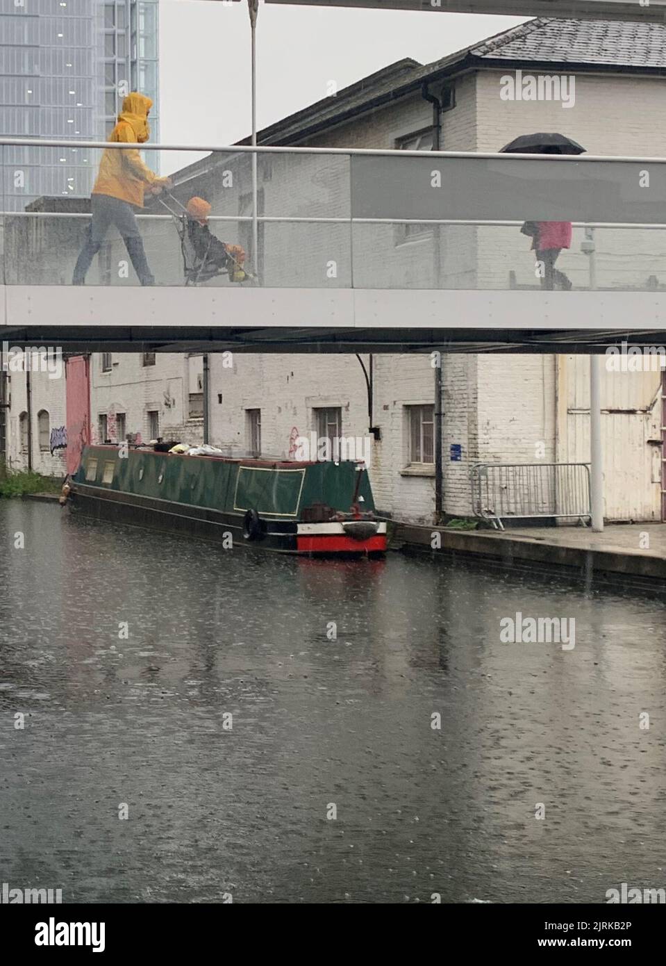 Les voyageurs se réfugient sous des parasols en traversant un pont sur le canal de Paddington, dans l'ouest de Londres, pendant une averse de pluie. Le bureau du met a émis un avertissement jaune pour les orages et les fortes pluies dans le sud et l'est de l'Angleterre, les conditions de conduite pouvant être affectées par les projections d'eau, les eaux stagnantes et même la grêle, ainsi que les retards possibles dans les services ferroviaires, les coupures d'électricité, les inondations et les éclairs. Date de la photo: Jeudi 25 août 2022. Banque D'Images