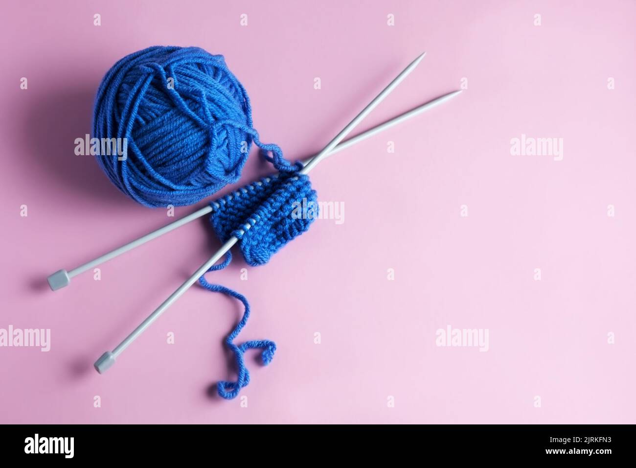 Laine bleue tricotée sur fond rose avec aiguilles à tricoter, passe-temps. Vue d'ensemble Banque D'Images