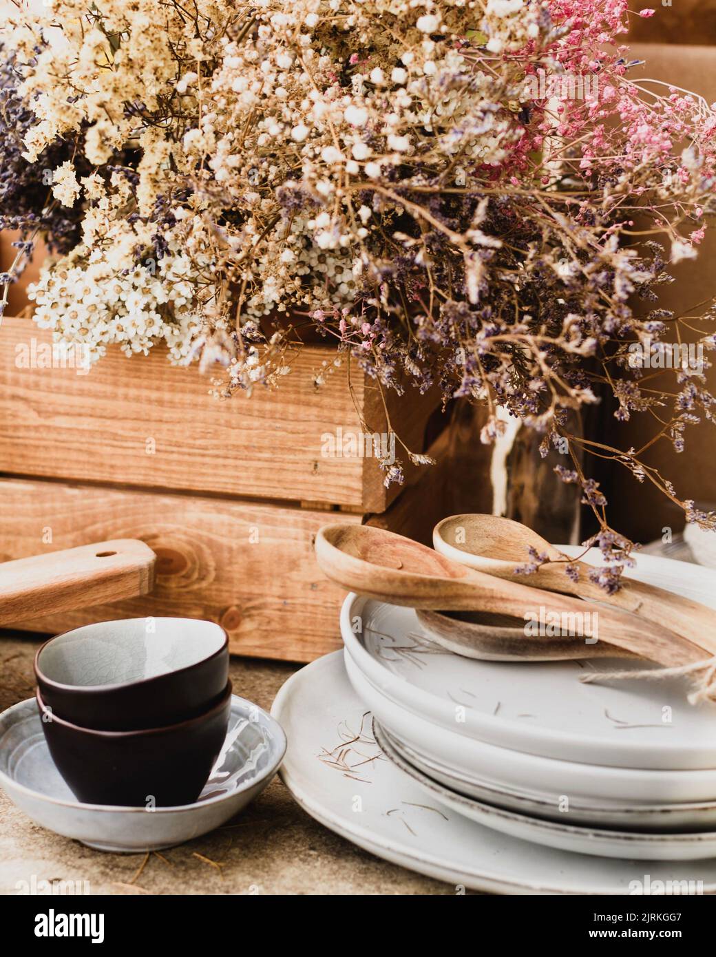Vaisselle en céramique noire et blanche avec des cuillères en bois à côté  de la caisse en chêne brun avec un bouquet luxuriant de fleurs sauvages  colorées sur la table dans le