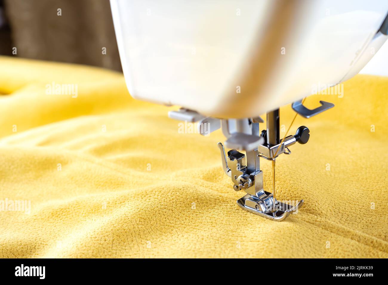 Machine à coudre moderne presser le pied avec le tissu et le fil jaune, gros plan, espace de copie. Processus de couture vêtements, rideaux, tissus d'ameublement. Affaires, loisirs, Banque D'Images