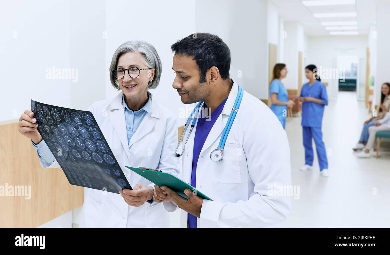 Deux médecins analysant l'IRM du cerveau du patient et diagnostiquant la maladie tout en se tenant dans le couloir de la clinique moderne pendant la journée de travail. équipe médicale Banque D'Images