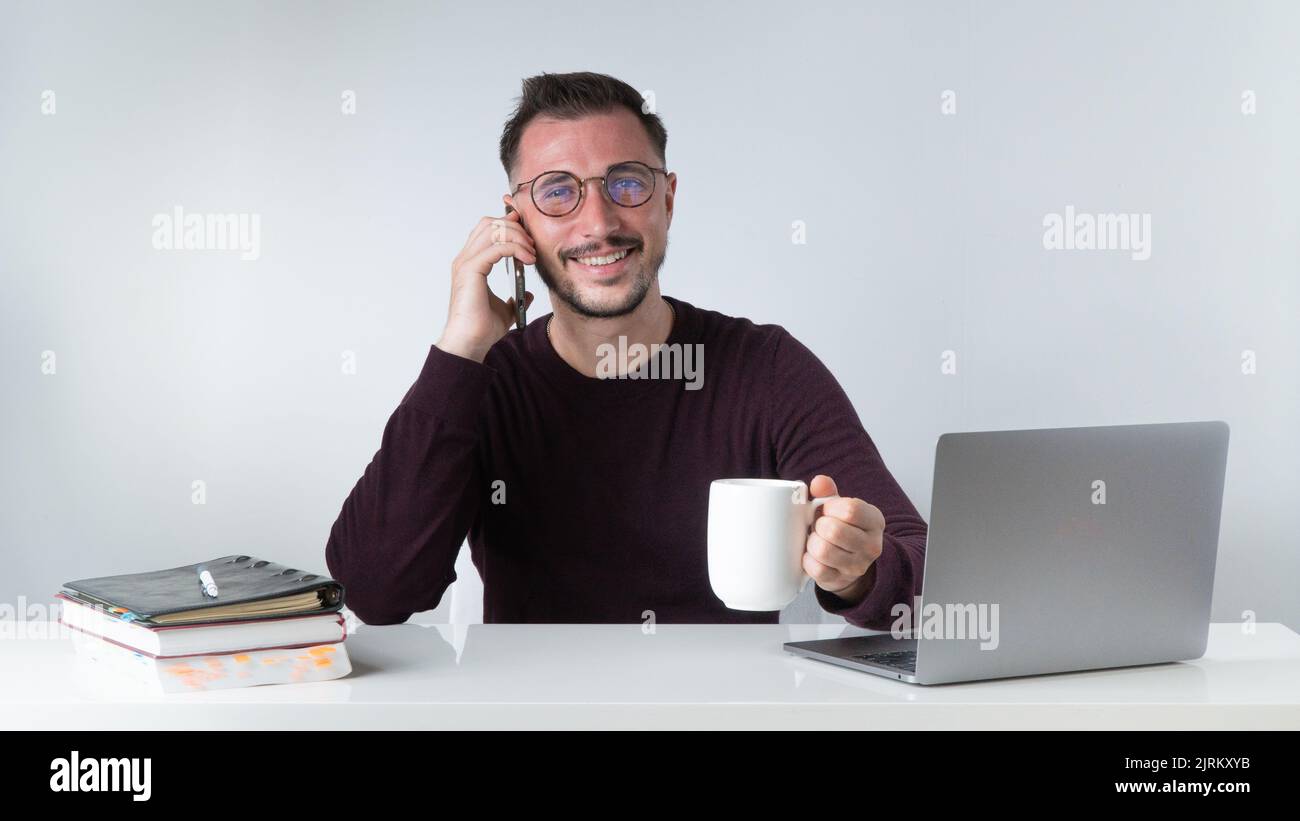 Un homme travaille sur un ordinateur portable avec un téléphone à la main et une tasse de café Banque D'Images