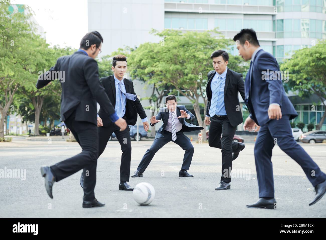 Des hommes d'affaires asiatiques séduits portant des costumes classiques se sont rassemblés après le travail à l'extérieur et ont soulagé le stress par un match de football Banque D'Images