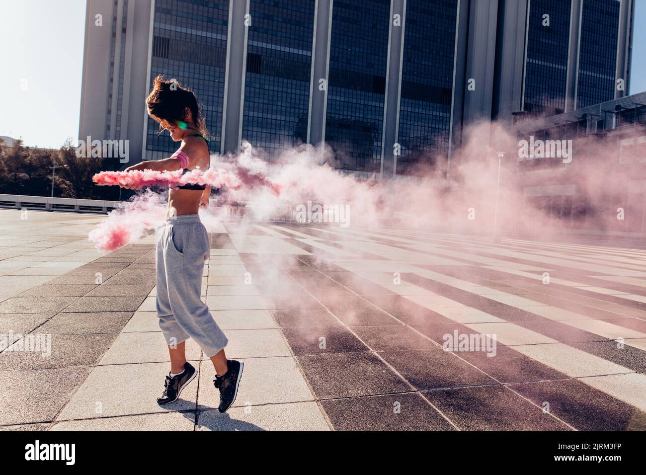 Femme tenant une grenade de fumée colorée à l'extérieur de la ville. Urban sportswoman avec bâtonnets de fumée. Banque D'Images