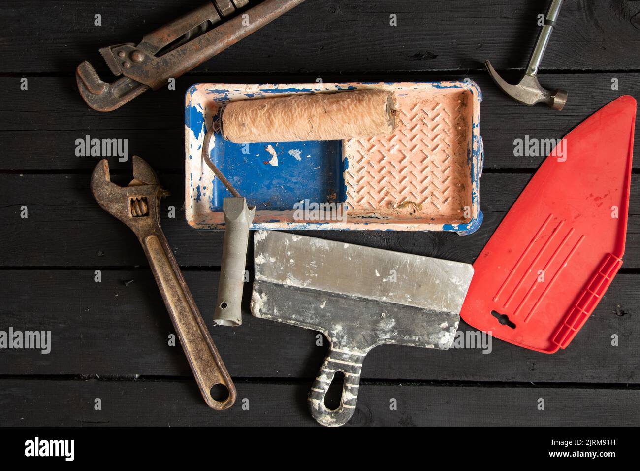 clé à gaz rouleau de marteau dans la peinture dans un plateau et une spatule reposent sur un plancher en bois noir, outils de réparation, kit d'outils de réparation Banque D'Images