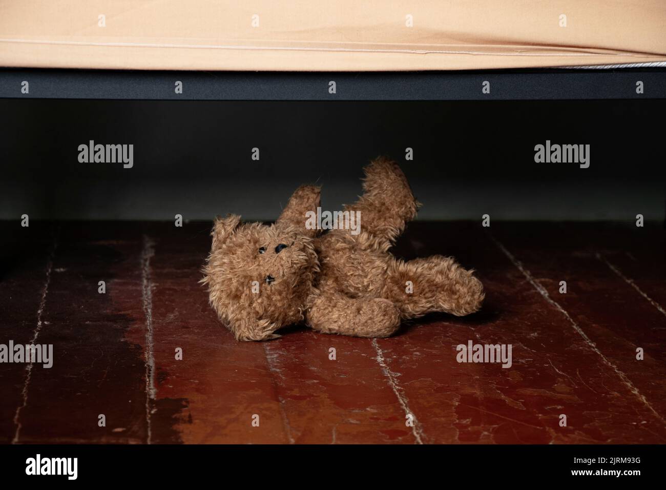 par le lit sur le sol dans la chambre de la maison se trouve un ours en peluche brun, un ours en peluche sous le lit sur le sol dans la nuit Banque D'Images