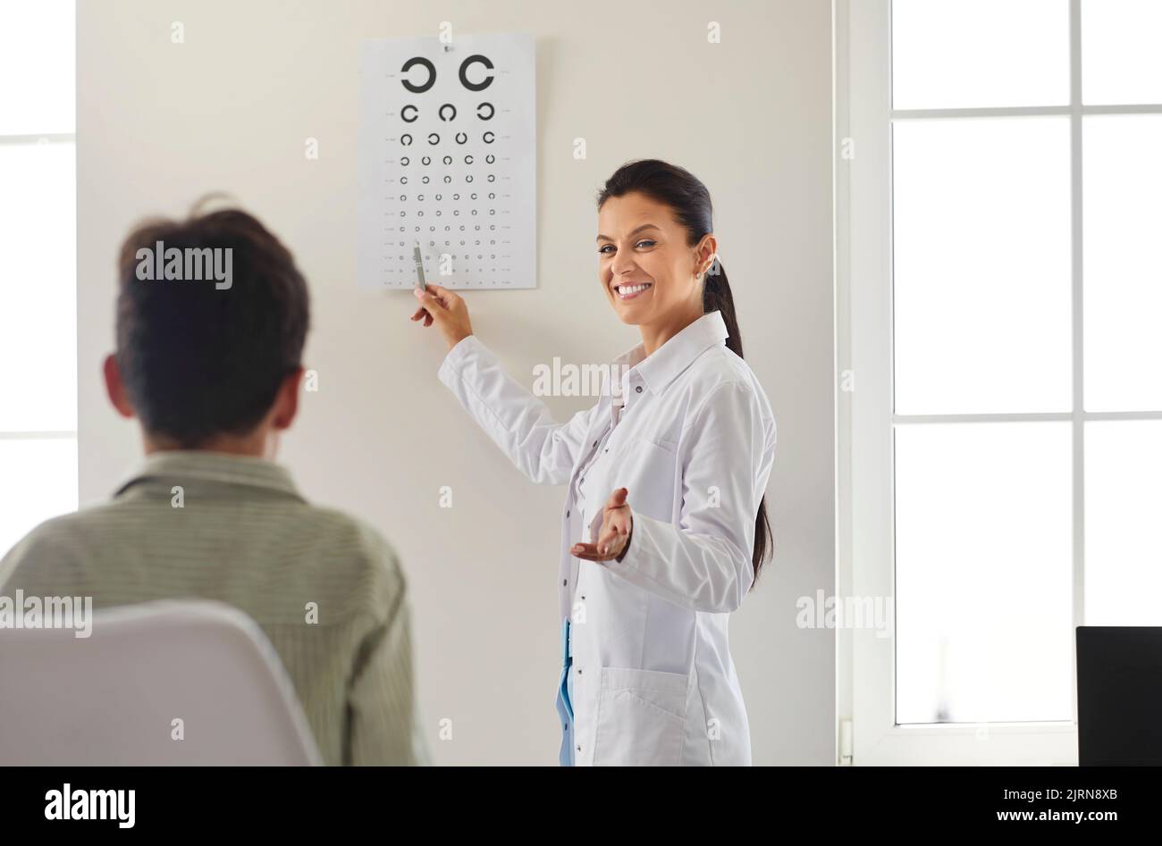 Un ophtalmologiste heureux qui teste la vue de l'enfant, qui pointe vers le graphique des yeux et sourit Banque D'Images