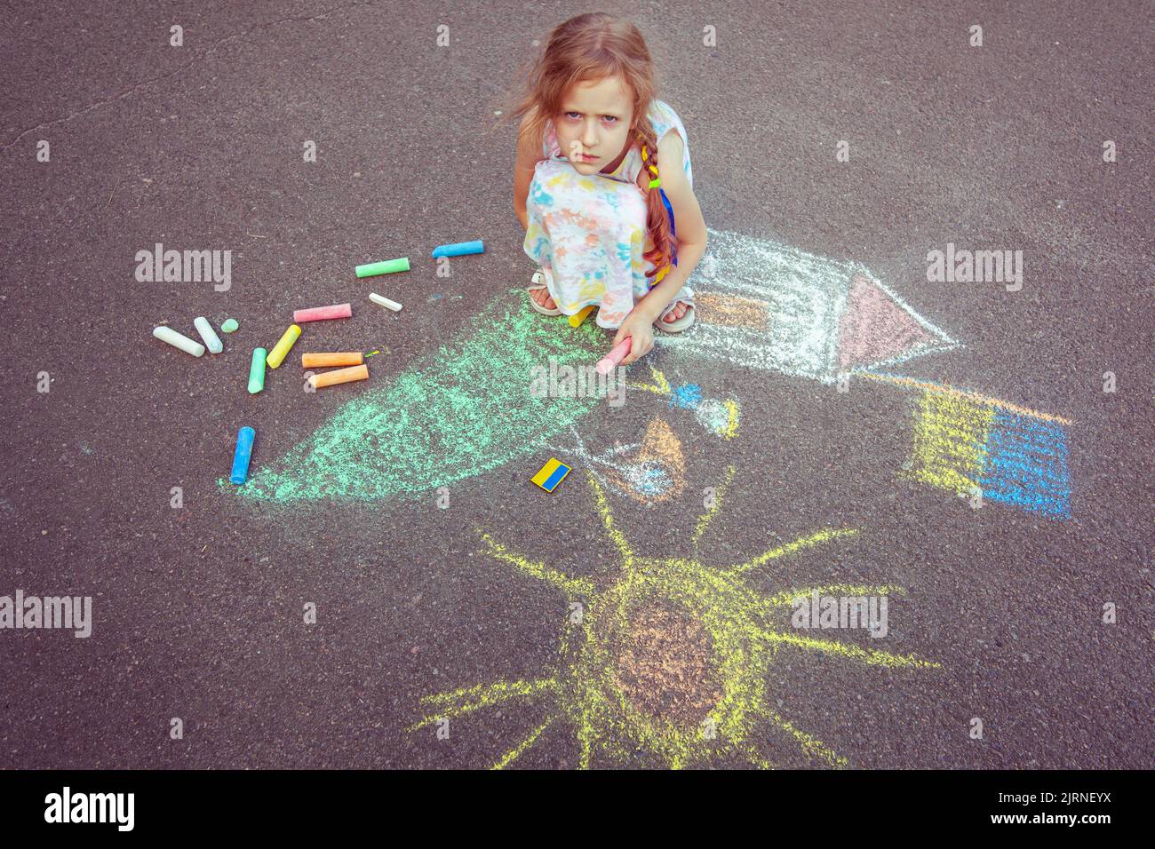 Une fille ukrainienne dessine les dessins des enfants avec de la craie sur le trottoir. Banque D'Images