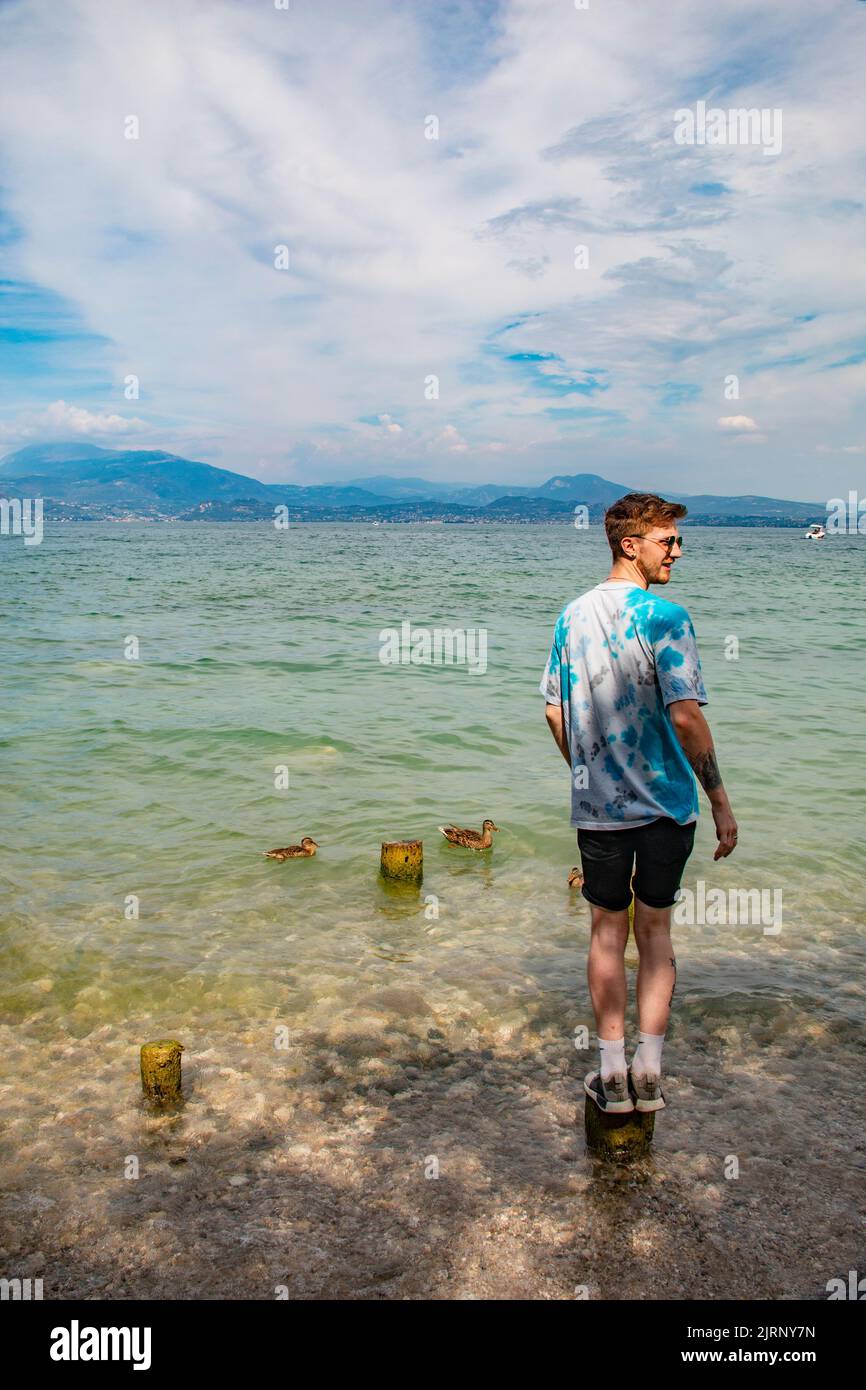 Beau jeune homme en équilibre sur le vieux pôle de la jetée sur le lac de Garde, Sirmione, Brescia, Italie Banque D'Images