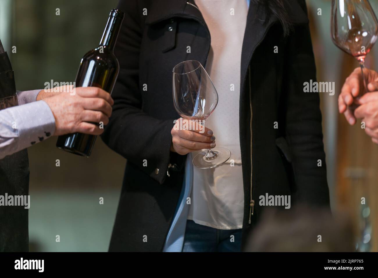 Vue rapprochée des mains masculines qui déversent du vin rouge d'une bouteille dans un verre de vin d'un jeune couple, touristes sur la visite des caves à vin authentiques Banque D'Images