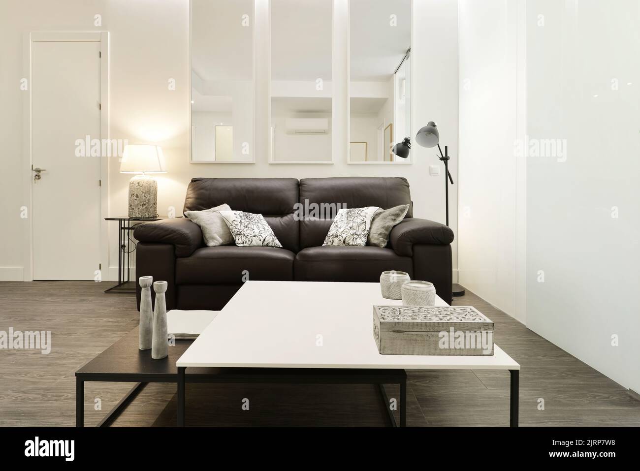 Salle de séjour avec canapé en cuir brun foncé dans une chambre légèrement décorée avec tables en bois carrées noires et blanches Banque D'Images
