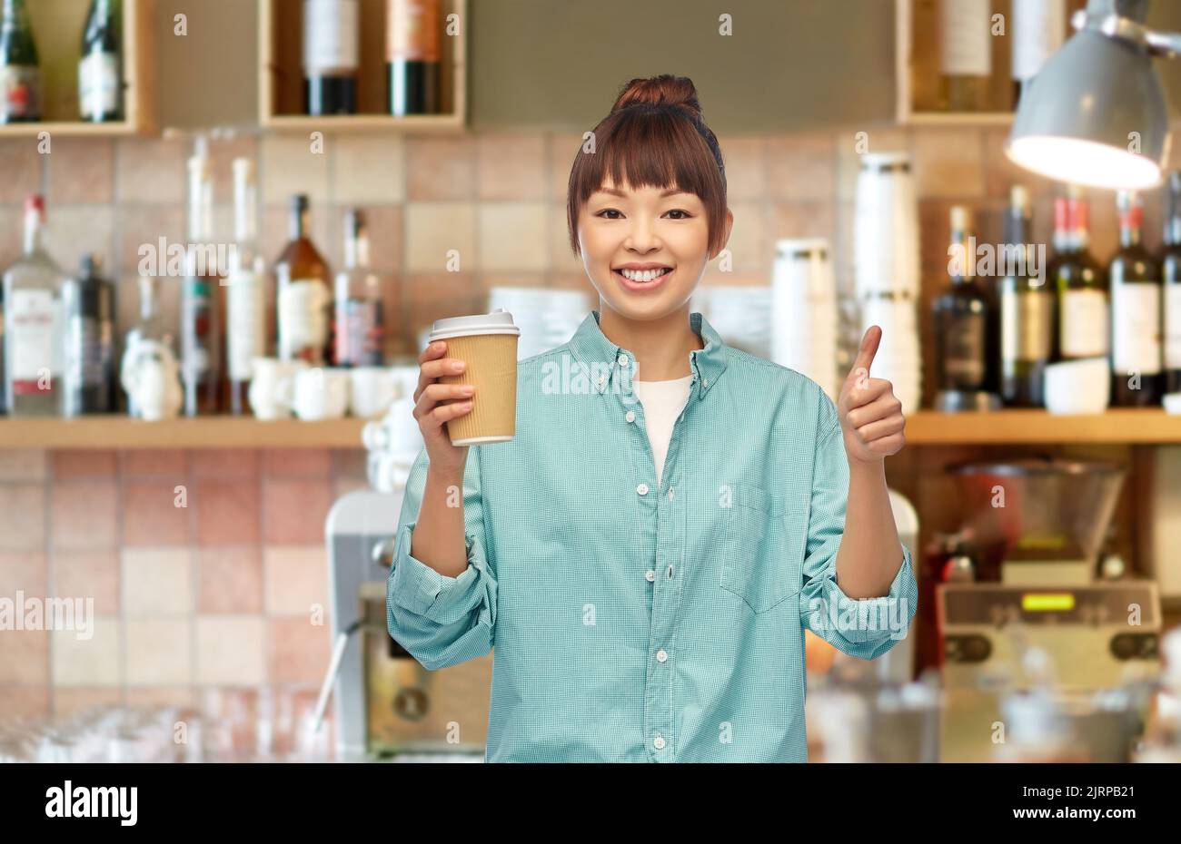 femme asiatique avec un café montrant les pouces au bar Banque D'Images
