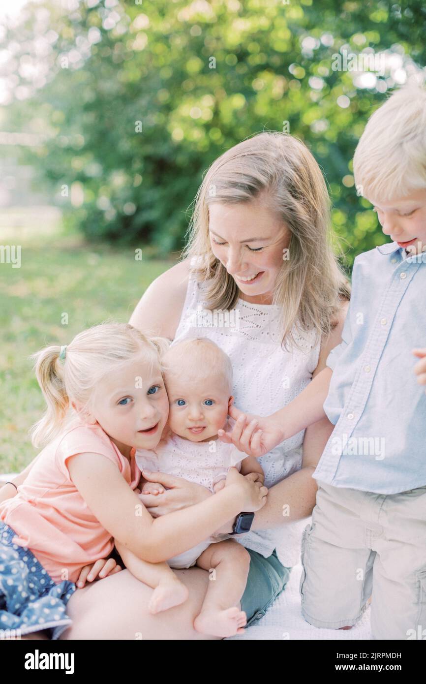 Blonde, la mère caucasienne est assise avec trois enfants dans le parc souriant. Banque D'Images