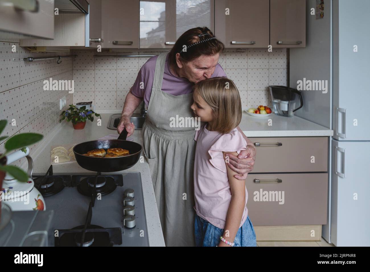 Une femme âgée dans la cuisine friture des tartes avec sa petite-fille. Banque D'Images