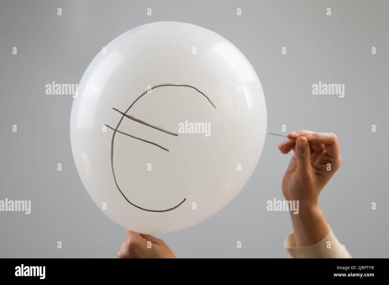 Une femme éclate avec une aiguille un ballon avec l'inscription euro. Banque D'Images