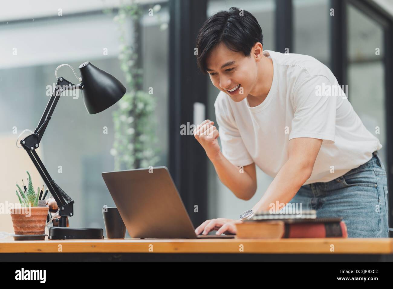 Un homme asiatique heureux utilisant un ordinateur portable tout en ayant une bonne nouvelle de travailler au bureau Banque D'Images