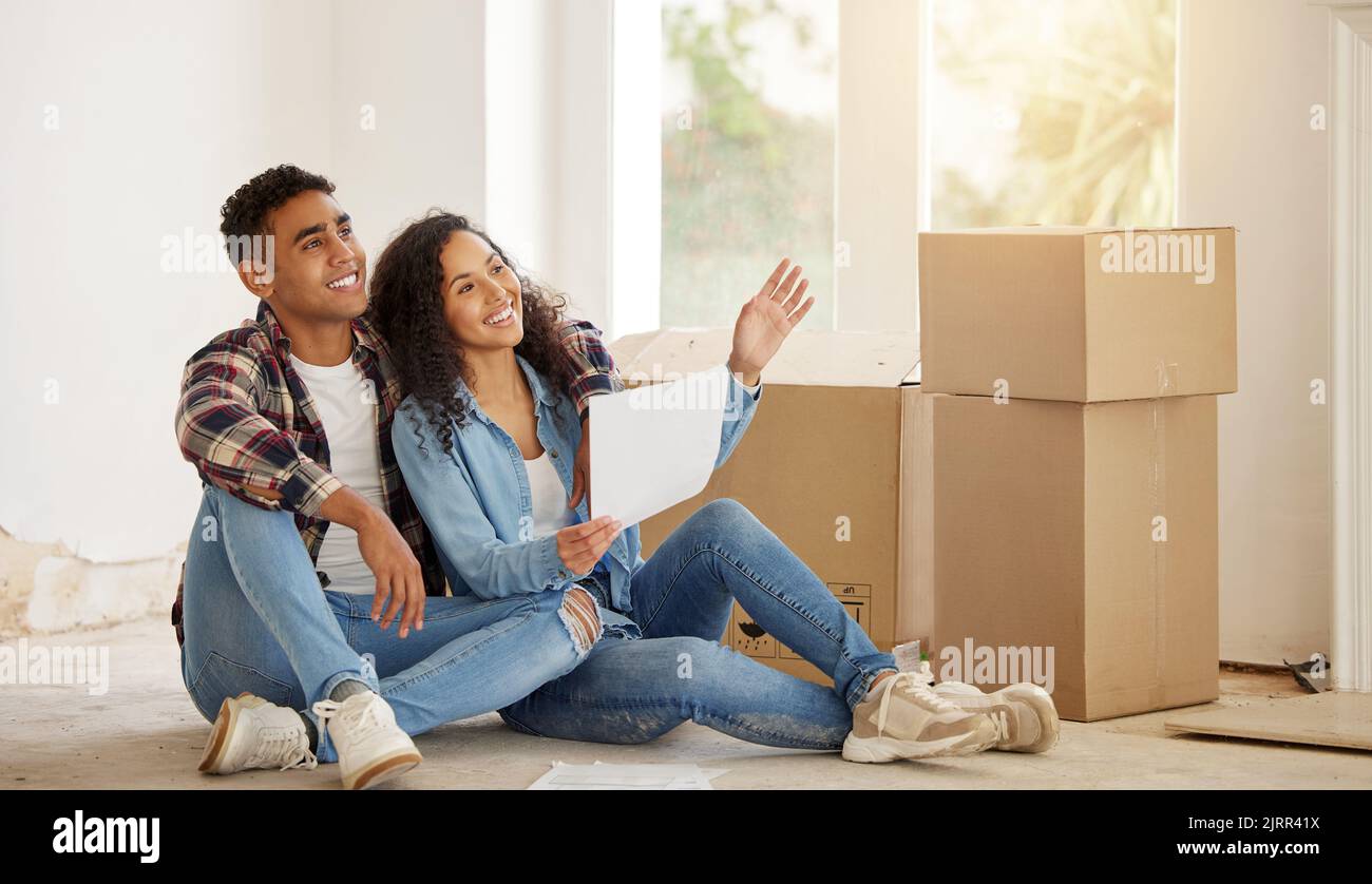 Couple heureux sur le plancher de leur nouvelle propriété ou maison dans le salon avec boîte en arrière-plan. Le propriétaire de l'immobilier sourit à l'intérieur du salon Banque D'Images