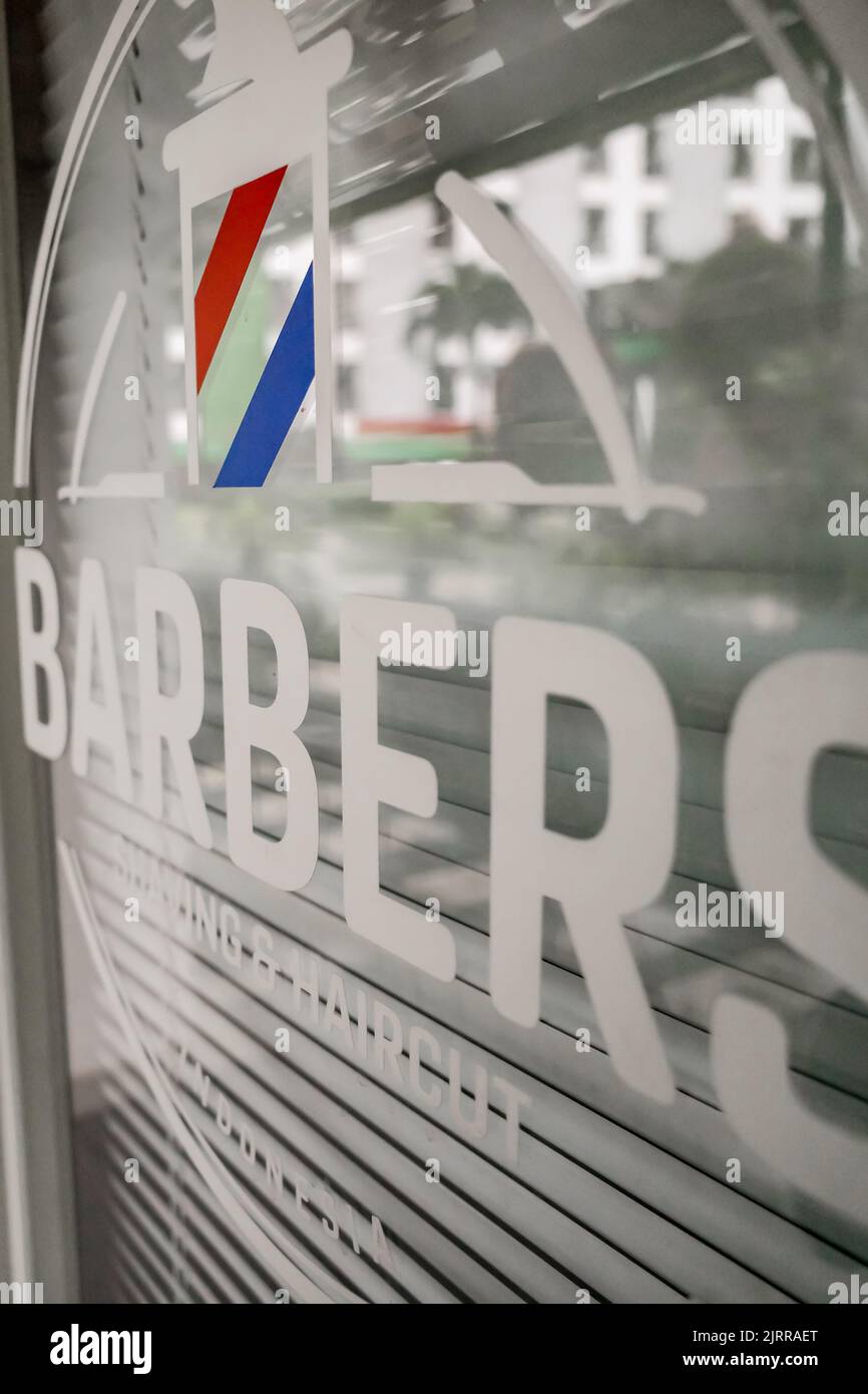 Autocollant de nom de salon de coiffure sur la porte vitrée d'entrée avec logo à rayures rouges, blanches et bleues Banque D'Images