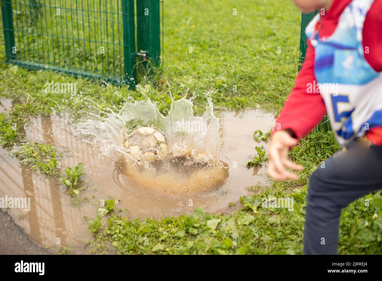 L'enfant a jeté le ballon dans la flaque. Frappez l'eau. Jeu Splash. Garçon fait jeter. Banque D'Images