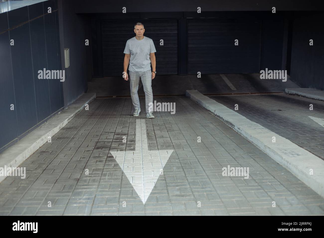 Pleine longueur d'homme d'affaires confiant debout sur l'entrée de stationnement sur la flèche blanche pointant vers la sortie, fond gris automatique de portes. Voiture souterraine Banque D'Images